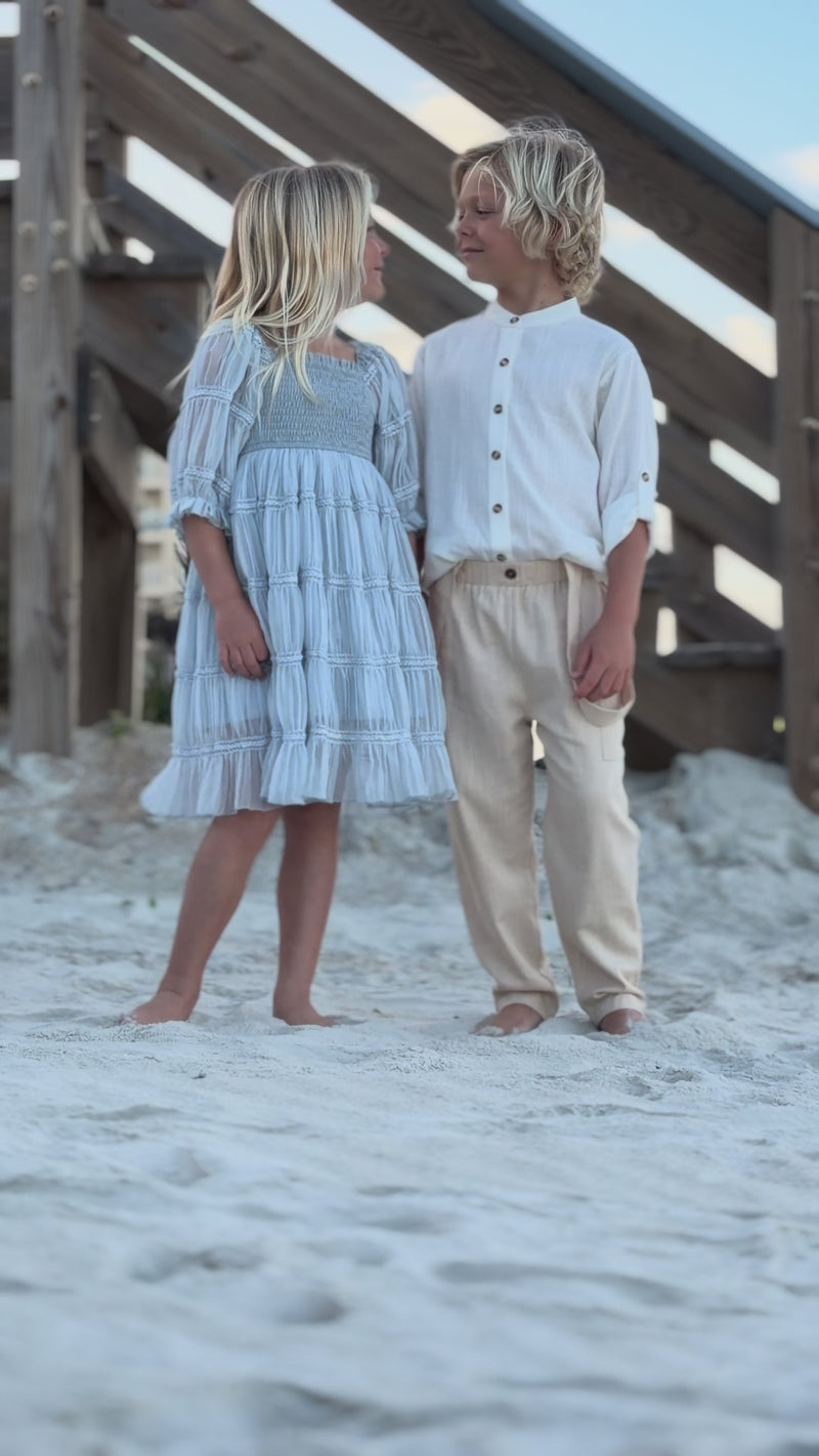 Video of girl wearing Indie Blue Karina Dress Blue Chiffon and Boy wearing Ty Shirt White Linen and Finn Pants walking together on the beach